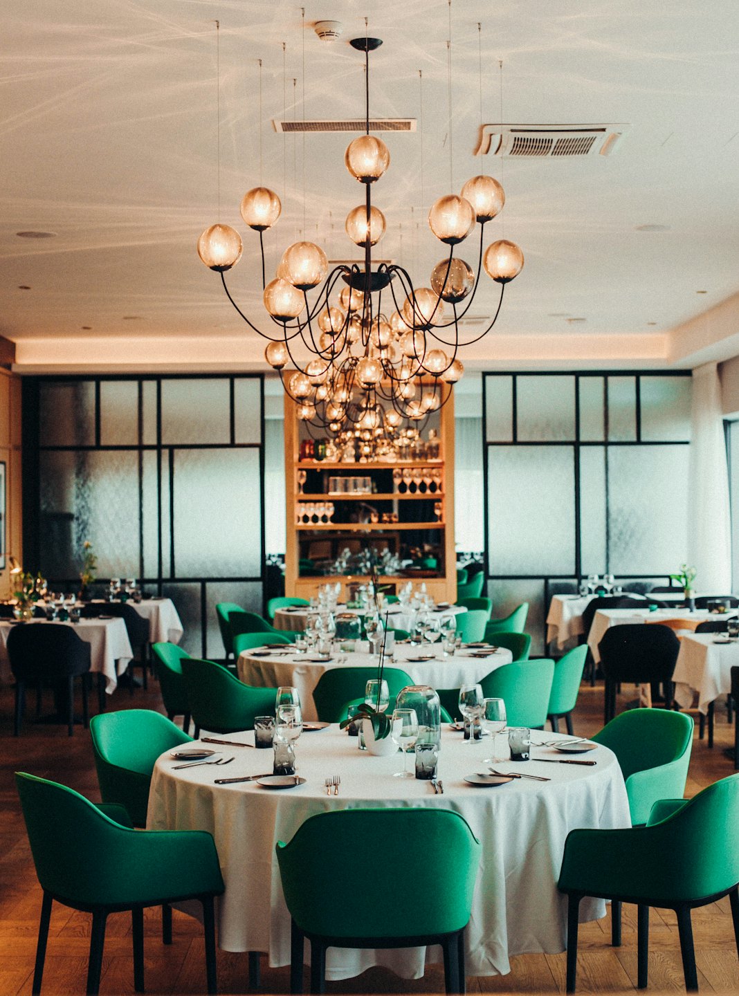 Eleganter Restaurant-Speisesaal mit runden Tischen und grünen Stühlen.