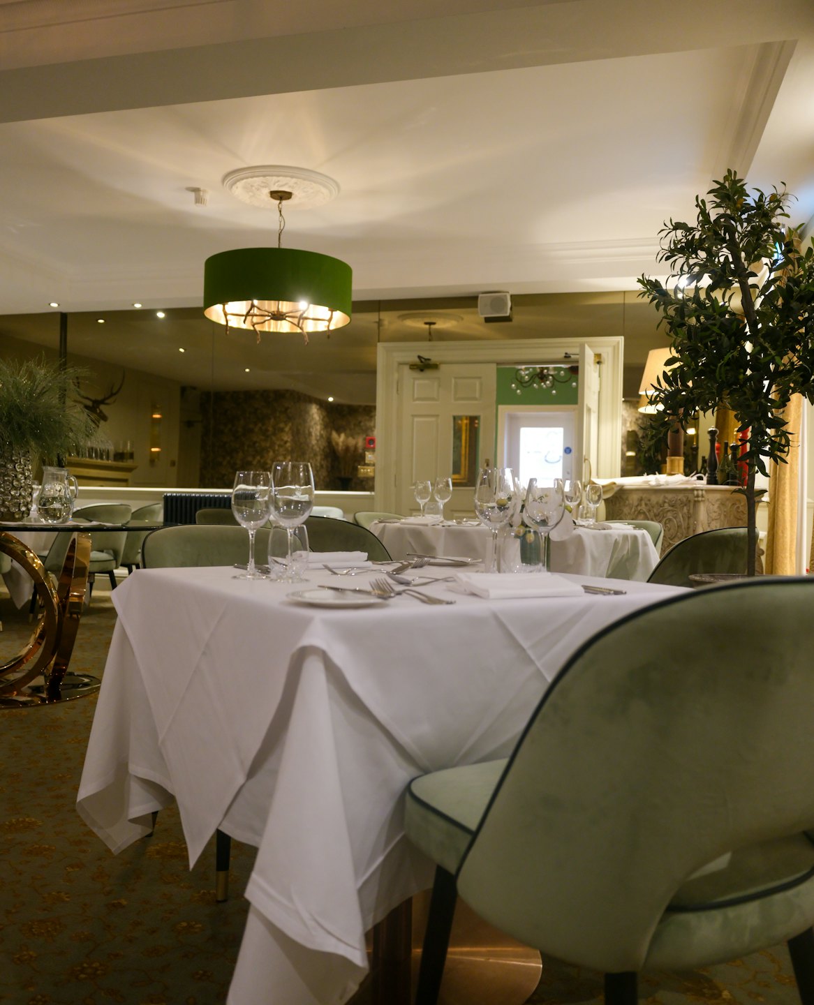Elegantes leeres Gourmetrestaurant mit gedeckten Tischen und grünen Stühlen.